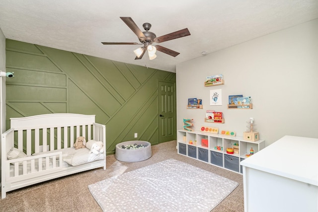 carpeted bedroom featuring a textured ceiling, a nursery area, and ceiling fan