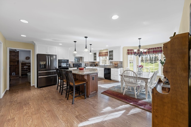 kitchen featuring white cabinetry, light stone countertops, black appliances, and a kitchen island