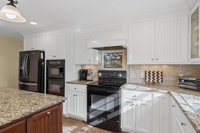 kitchen with custom exhaust hood, white cabinetry, decorative light fixtures, black appliances, and backsplash