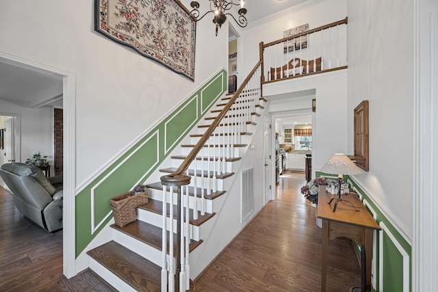 stairs with hardwood / wood-style flooring, ornamental molding, a towering ceiling, and a chandelier