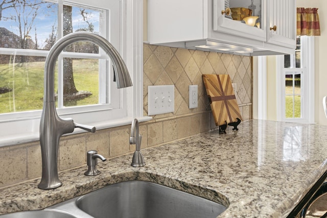 interior details featuring light stone counters, backsplash, sink, and white cabinets