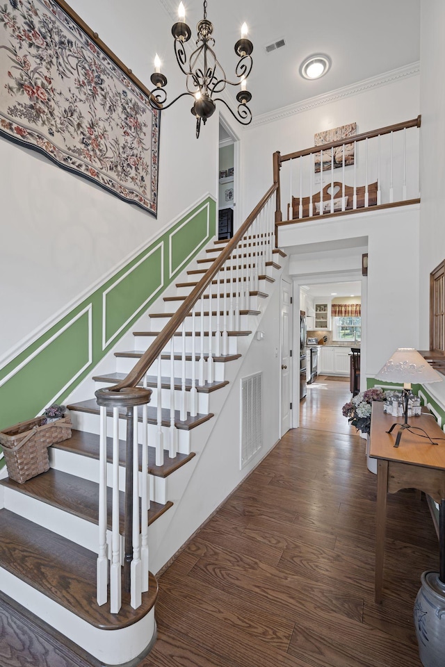 stairs with a towering ceiling, wood-type flooring, a notable chandelier, and ornamental molding