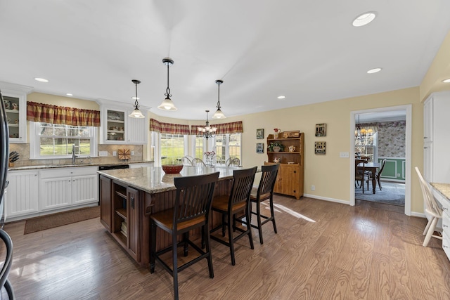 kitchen featuring a breakfast bar, hanging light fixtures, a notable chandelier, an island with sink, and white cabinets