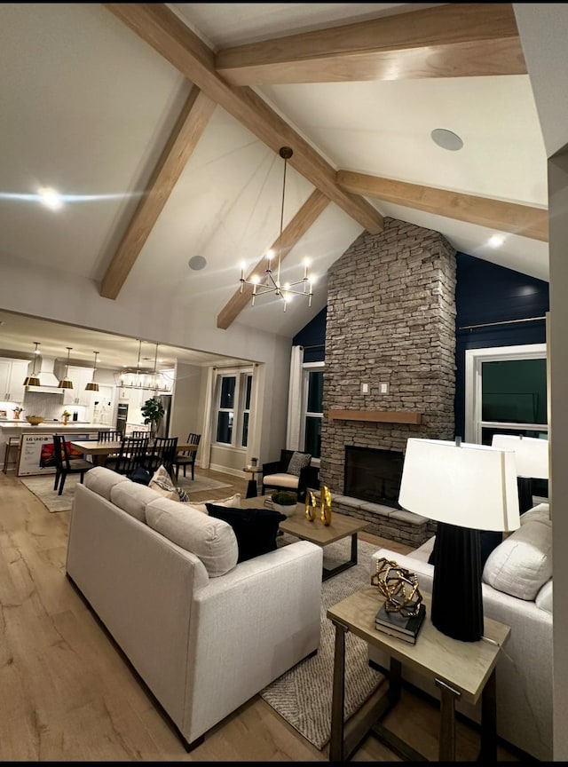 living room featuring beamed ceiling, a stone fireplace, a chandelier, and light hardwood / wood-style floors