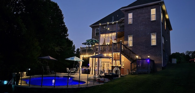 back house at dusk featuring a balcony and a yard