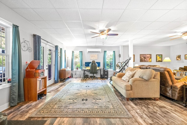 living room with hardwood / wood-style flooring, ceiling fan, a paneled ceiling, and a wall unit AC