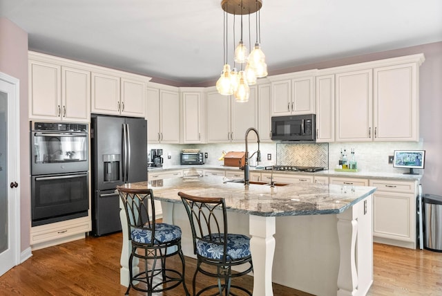 kitchen with light stone counters, a center island with sink, white cabinets, and appliances with stainless steel finishes