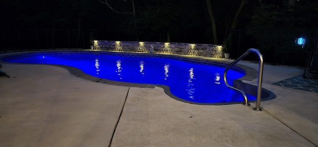 pool at night featuring a patio area