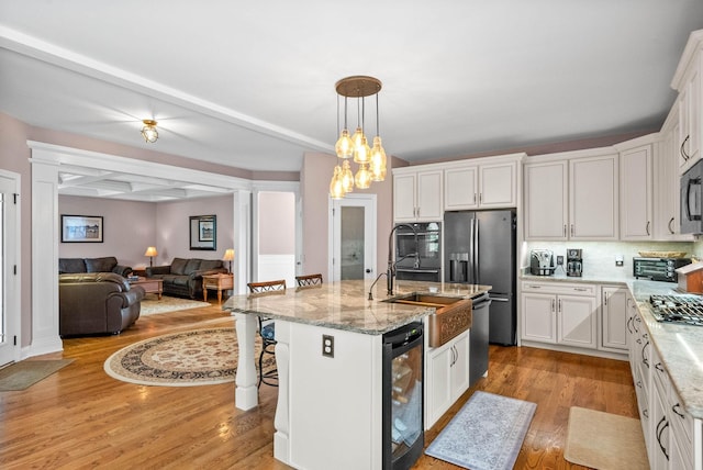 kitchen featuring pendant lighting, white cabinetry, wine cooler, black appliances, and a center island with sink