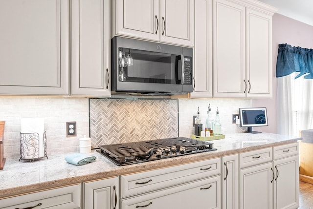 kitchen featuring stainless steel gas stovetop, light stone countertops, white cabinets, and decorative backsplash