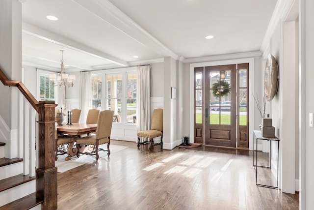 entryway with a notable chandelier, beam ceiling, wood-type flooring, and ornamental molding