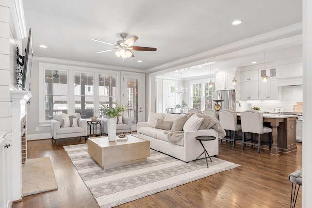 living room featuring ornamental molding, dark hardwood / wood-style floors, ceiling fan with notable chandelier, and a fireplace