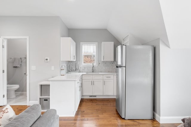 kitchen featuring sink, white cabinetry, light wood-type flooring, stainless steel fridge, and decorative backsplash