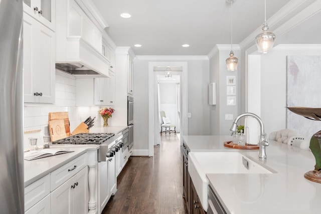 kitchen with sink, custom exhaust hood, hanging light fixtures, ornamental molding, and white cabinets