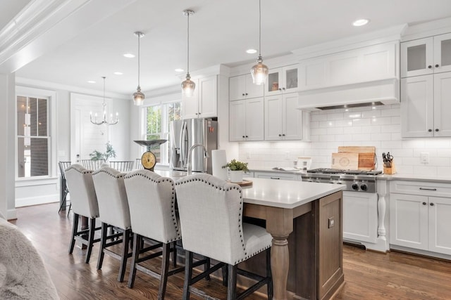 kitchen featuring hanging light fixtures, stainless steel appliances, an island with sink, white cabinets, and custom exhaust hood