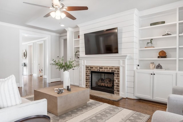 living room featuring dark wood-type flooring, a brick fireplace, ornamental molding, built in features, and ceiling fan