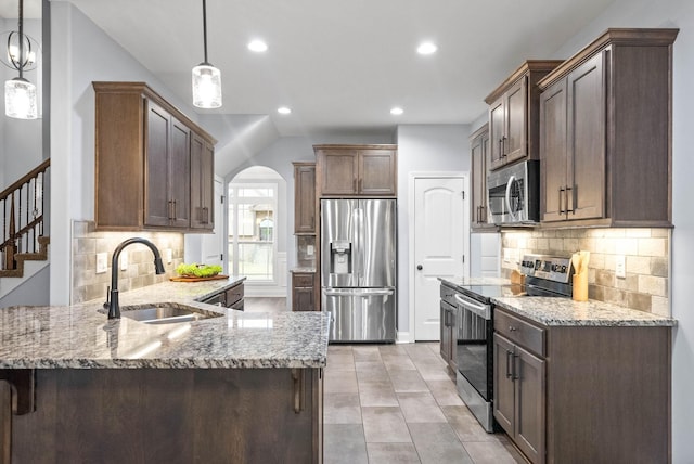 kitchen with light stone countertops, appliances with stainless steel finishes, a peninsula, arched walkways, and a sink