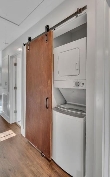 clothes washing area featuring hardwood / wood-style flooring, stacked washer and clothes dryer, and a barn door