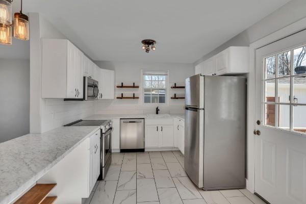 kitchen featuring sink, hanging light fixtures, appliances with stainless steel finishes, light stone countertops, and white cabinets