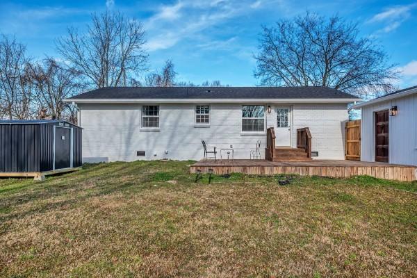 rear view of house featuring a yard, a deck, and a storage unit