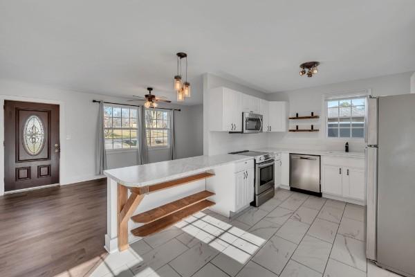 kitchen with plenty of natural light, appliances with stainless steel finishes, hanging light fixtures, and white cabinets