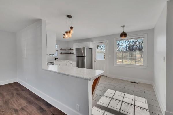 kitchen with hanging light fixtures, white cabinets, stainless steel refrigerator, and kitchen peninsula