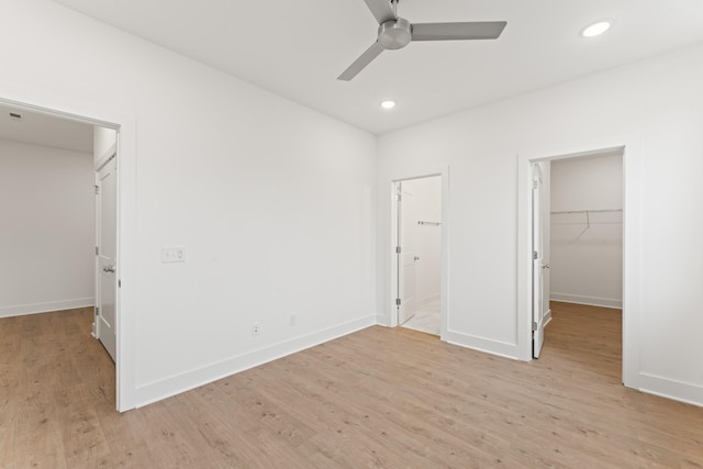 unfurnished bedroom with connected bathroom, a spacious closet, a closet, ceiling fan, and light hardwood / wood-style floors