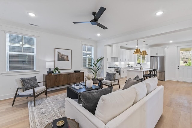 living room featuring ceiling fan, light hardwood / wood-style floors, sink, and a wealth of natural light