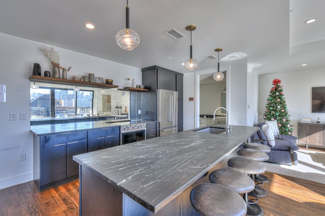 kitchen with appliances with stainless steel finishes, pendant lighting, sink, dark hardwood / wood-style flooring, and a center island with sink