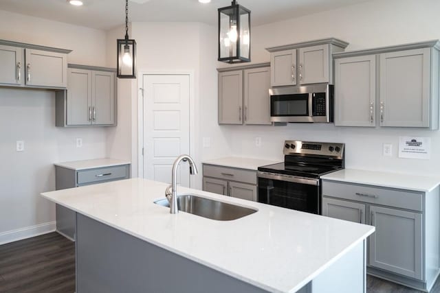 kitchen with sink, appliances with stainless steel finishes, gray cabinets, pendant lighting, and a kitchen island with sink