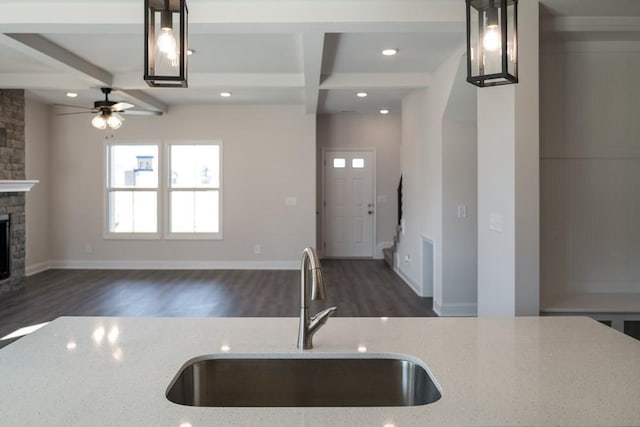 kitchen with pendant lighting, a fireplace, beamed ceiling, sink, and light stone counters