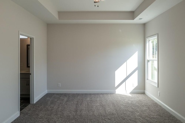 spare room with a raised ceiling and dark colored carpet