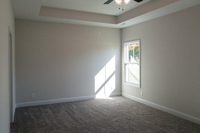 unfurnished room featuring a tray ceiling, dark carpet, and ceiling fan