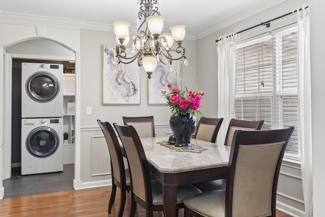 dining area featuring ornamental molding, stacked washer and clothes dryer, dark hardwood / wood-style floors, and a notable chandelier