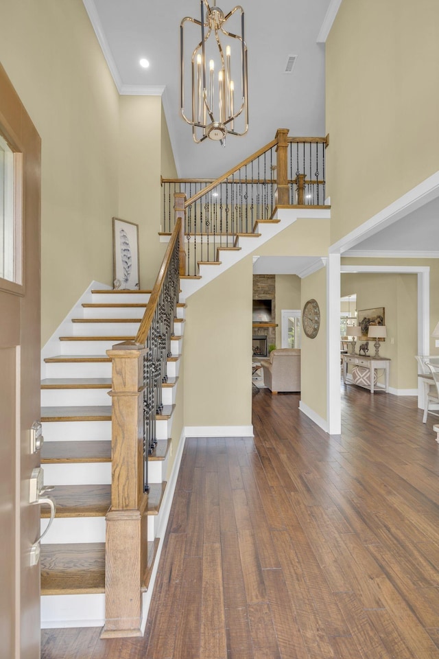 stairs featuring crown molding, a notable chandelier, a fireplace, hardwood / wood-style floors, and a high ceiling