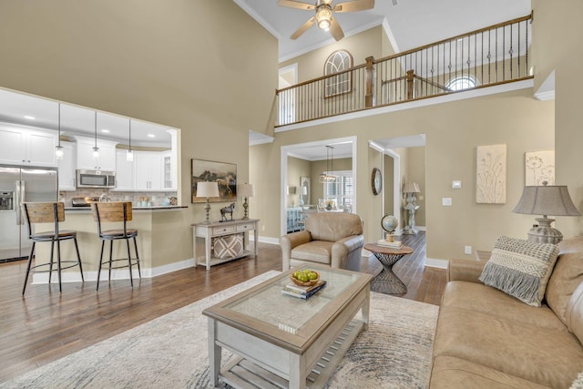 living room with hardwood / wood-style flooring, ceiling fan, crown molding, and a high ceiling