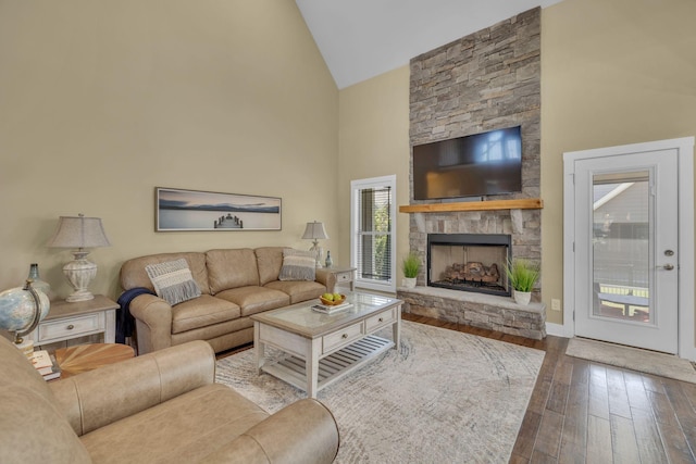 living room with hardwood / wood-style flooring, a stone fireplace, and high vaulted ceiling