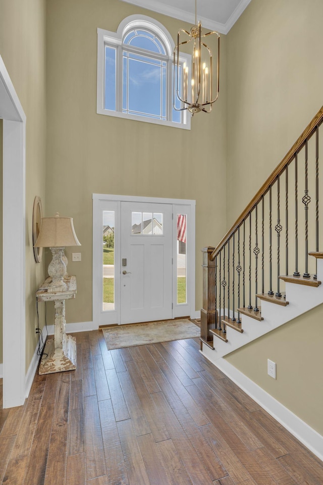 entryway with hardwood / wood-style flooring, ornamental molding, a chandelier, and a towering ceiling