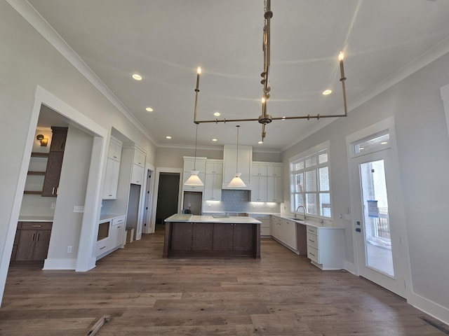 kitchen with hanging light fixtures, ornamental molding, a center island, and dark hardwood / wood-style floors