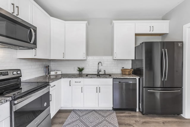 kitchen with appliances with stainless steel finishes, sink, dark stone countertops, and white cabinets