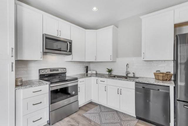 kitchen featuring appliances with stainless steel finishes, sink, white cabinets, light stone countertops, and light hardwood / wood-style flooring