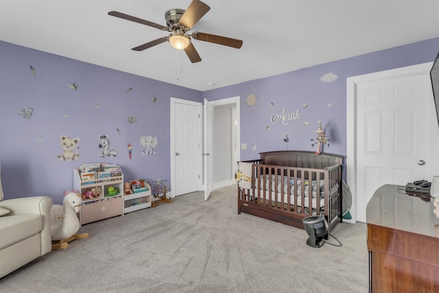 carpeted bedroom featuring ceiling fan and a crib