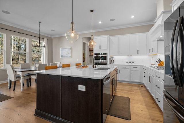 kitchen with sink, white cabinets, hanging light fixtures, stainless steel appliances, and a center island with sink