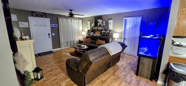 living area with ceiling fan, a textured ceiling, and wood finished floors