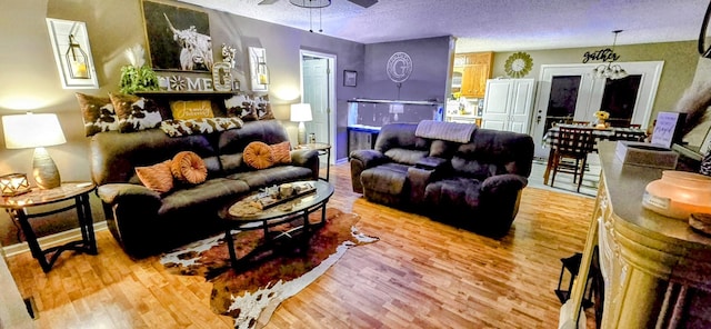 living room featuring a textured ceiling, ceiling fan, light wood finished floors, and baseboards