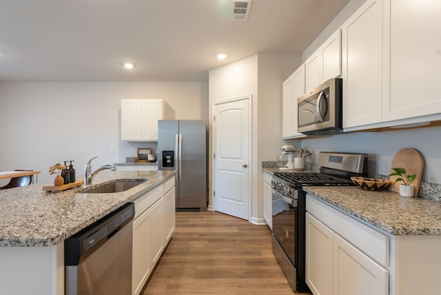 kitchen featuring appliances with stainless steel finishes, sink, white cabinets, a center island with sink, and light hardwood / wood-style flooring