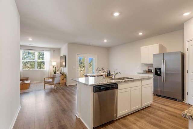 kitchen with sink, white cabinetry, light stone counters, appliances with stainless steel finishes, and an island with sink