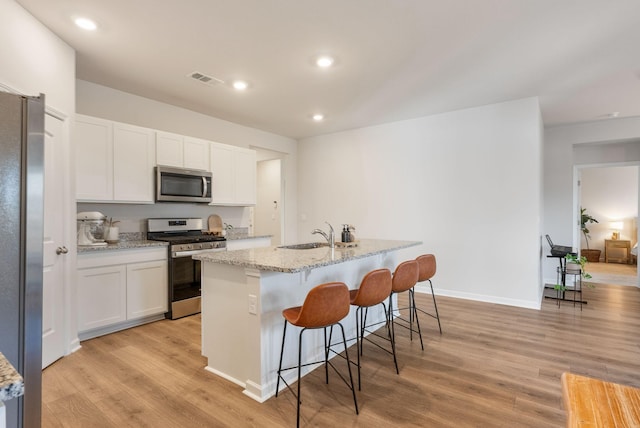 kitchen with white cabinetry, stainless steel appliances, light stone counters, light hardwood / wood-style floors, and an island with sink