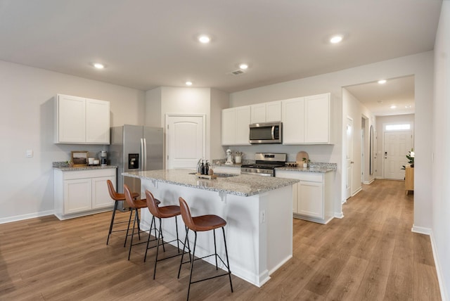 kitchen with stainless steel appliances, white cabinetry, and an island with sink