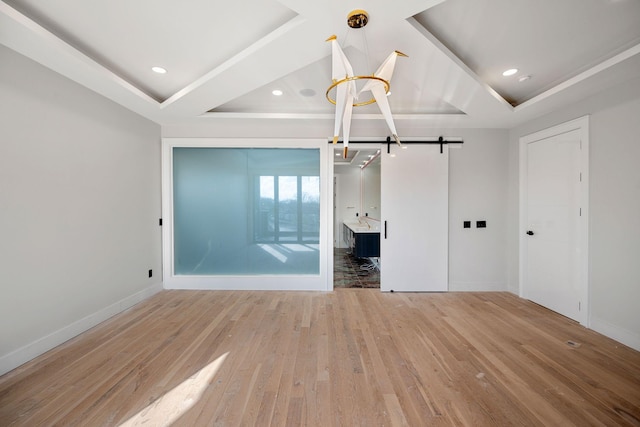 unfurnished bedroom featuring a raised ceiling, a barn door, and light hardwood / wood-style floors